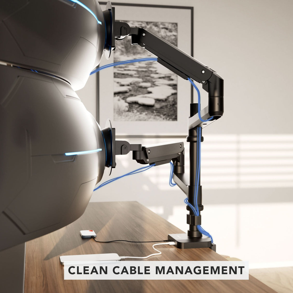 A wooden desk displays the Mount-It! Heavy-Duty Dual Stacking Monitor Mount with Pole & Gas Spring Arms, offering full motion flexibility and organized blue cables. A "CLEAN CABLE MANAGEMENT" label is seen, with black and white art on the wall behind.