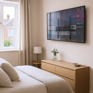 Modern bedroom featuring a flat-panel TV mounted with the Mount-It! Low Profile Slim TV Wall Mount Fixed TV Bracket, holding a 32-55 inch screen securely just over one inch from the wall for a sleek, space-saving look, with a light wood dresser, minimal decor, and natural light from a large window enhancing the clean, contemporary setup. Modern bedroom featuring a flat-panel TV mounted with the Mount-It! Low Profile Slim TV Wall Mount Fixed TV Bracket, holding a 32-55 inch screen securely just over one inch from the wall for a sleek, space-saving look, with a light wood dresser, minimal decor, and natural light from a large window enhancing the clean, contemporary setup.