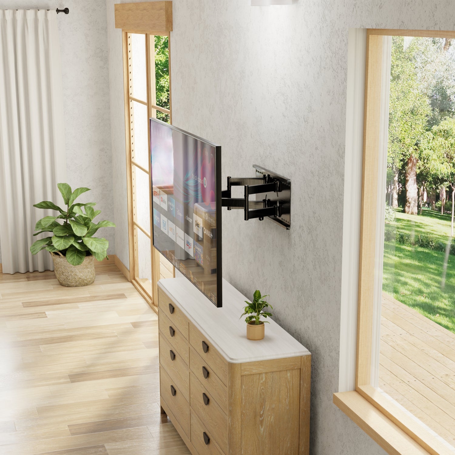 Heavy Duty Full Motion TV Wall Mount with Extension securely holding a large flat-screen television on a light-colored wall above a wooden cabinet with a plant, shown extended away from the wall in a bright room with large windows and natural light, illustrating the mount’s robust dual arm design, full swivel and tilt capabilities for optimal viewing angles and space-saving installation.