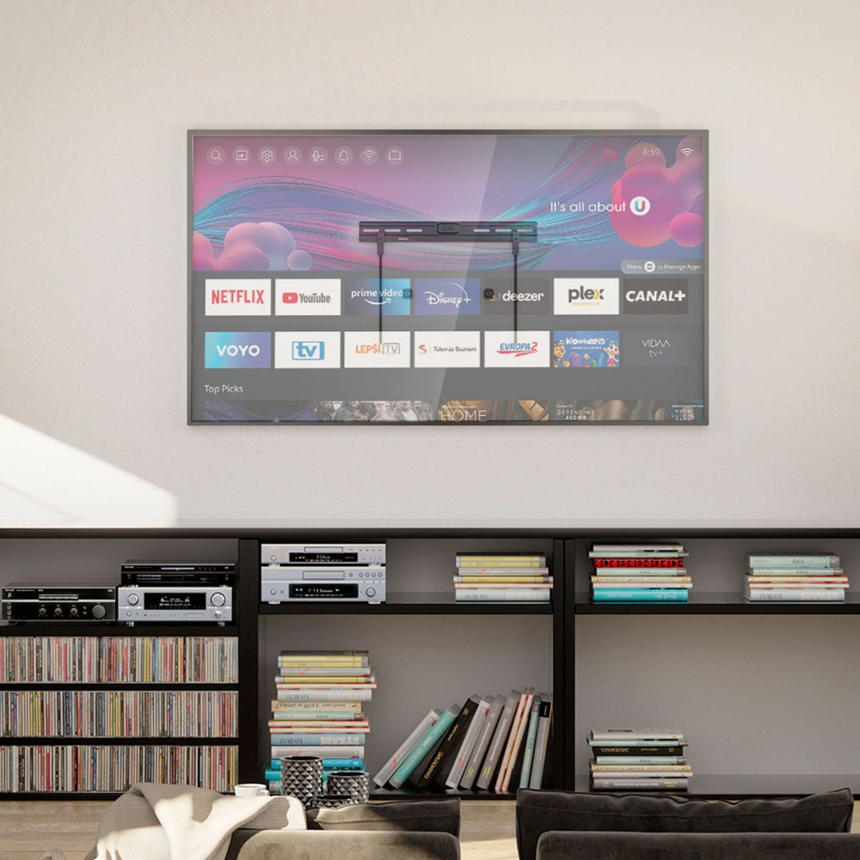 A flat-screen TV is mounted on a light wall using the Mount-It! No Stud TV Wall Mount, displaying a smart interface with Netflix, YouTube, and Plex. Shelves underneath hold books, audio gear, and vinyl records.