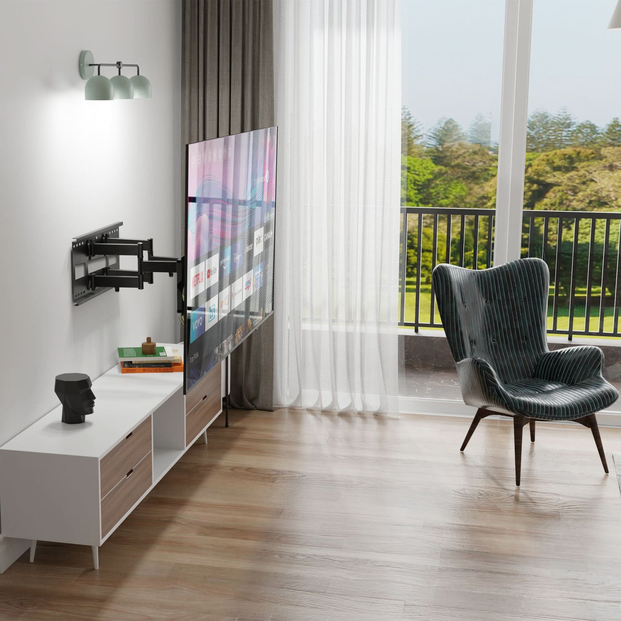 A modern living room features a Mount-It! Heavy Duty Dual Arm TV Wall Mount with Extra Long Extension holding the TV, a white media console with books and decor, striped armchair, large windows with sheer curtains, and a balcony overlooking greenery.