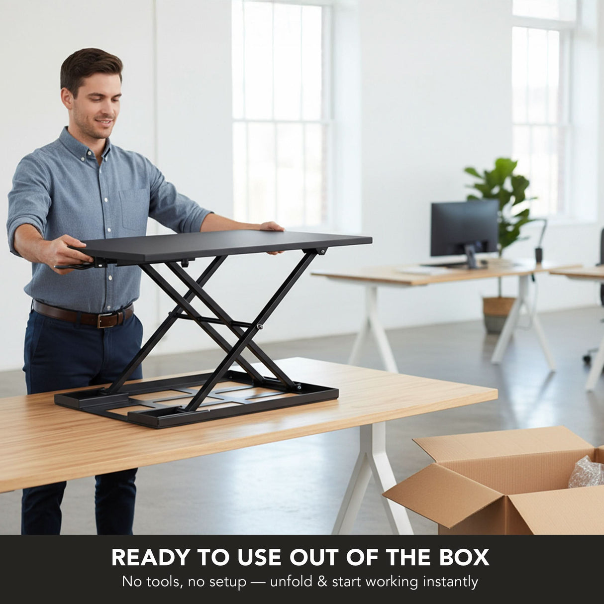 A man sets up a Mount-It! Height Adjustable X-Lift Standing Desk Converter on a wooden desk in a bright, modern office. Text reads: Ready to use out of the box—no tools or setup needed. Just unfold and start working instantly.