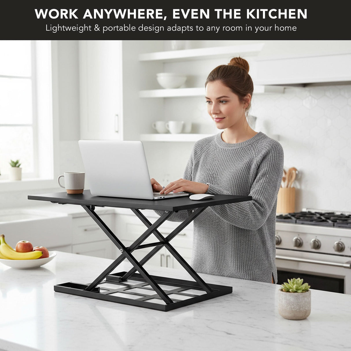 A woman uses her laptop on the Mount-It! Height Adjustable X-Lift Standing Desk Converter, placed on a white kitchen counter in a modern setting with shelves, kitchen items, and fruit bowl visible in the background.