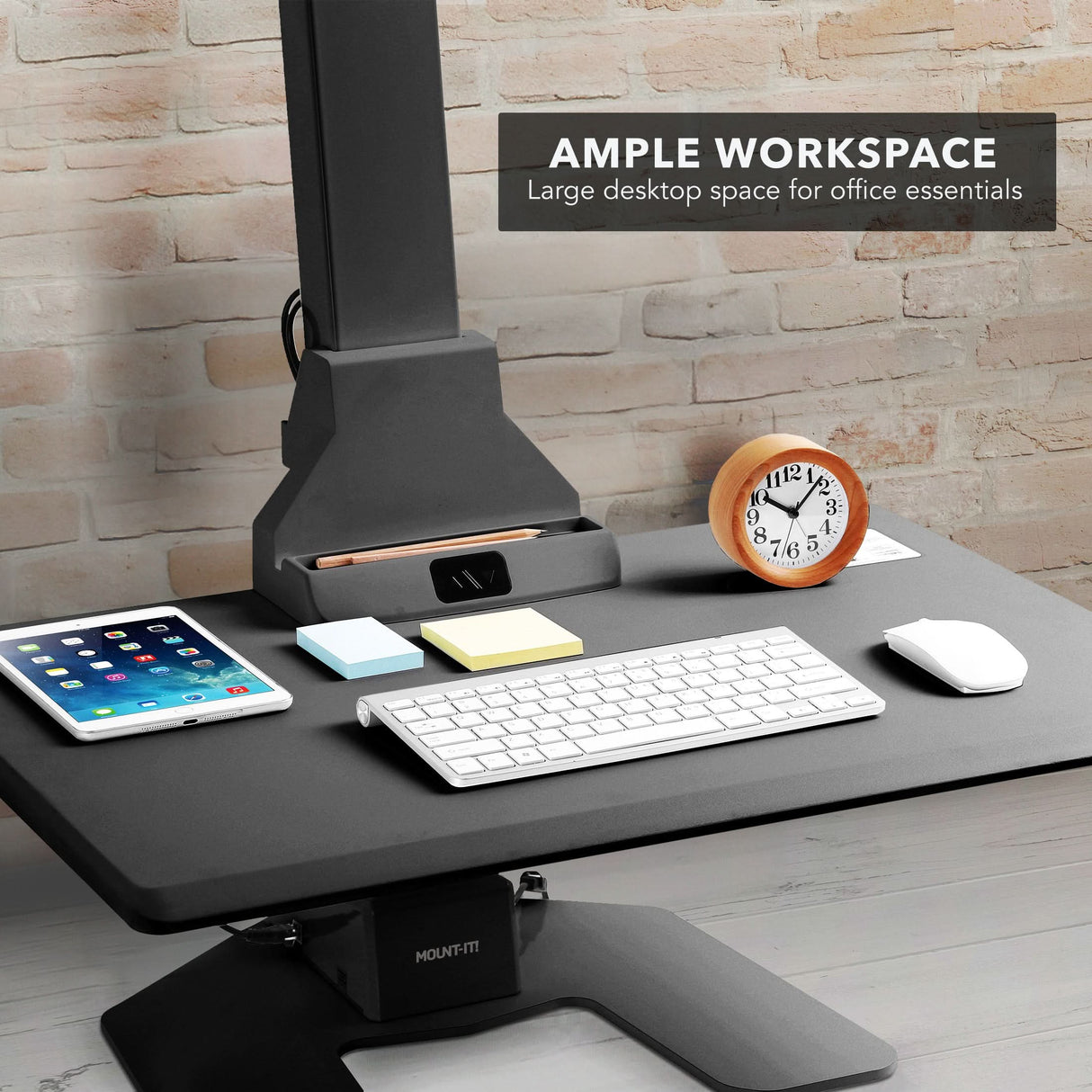 Black electric standing desk converter with office essentials on a wooden desk and brick wall background