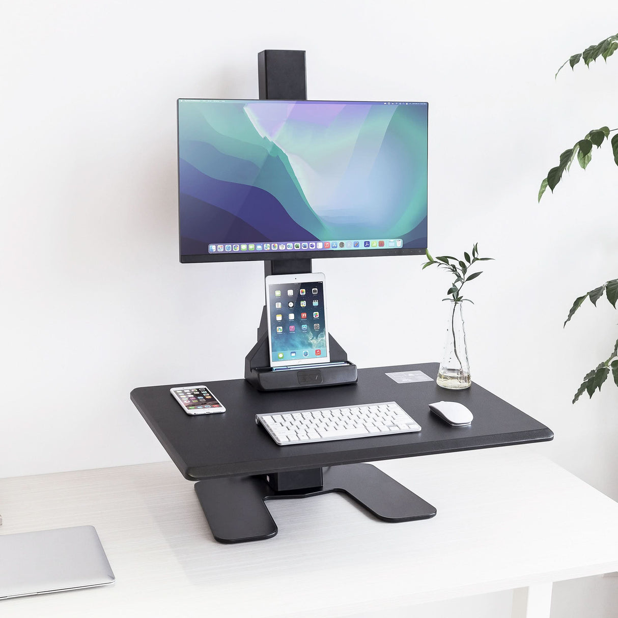 Black adjustable desk converter with computer monitor, tablet stand, keyboard, and mouse on a white surface.