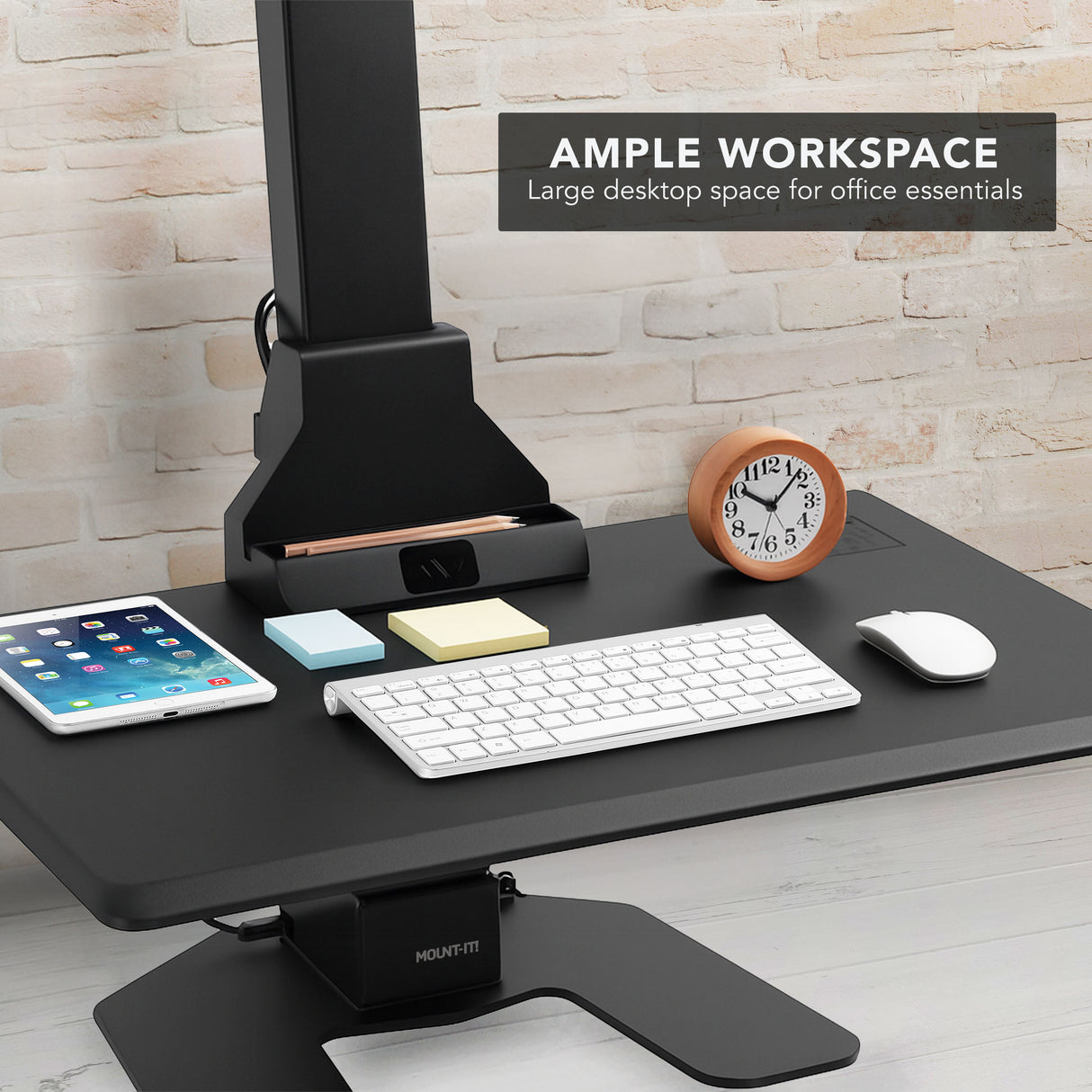 Electric Standing Desk Converter for 3 Monitors Black adjustable desk converter with office essentials on a light wood floor and stone wall background
