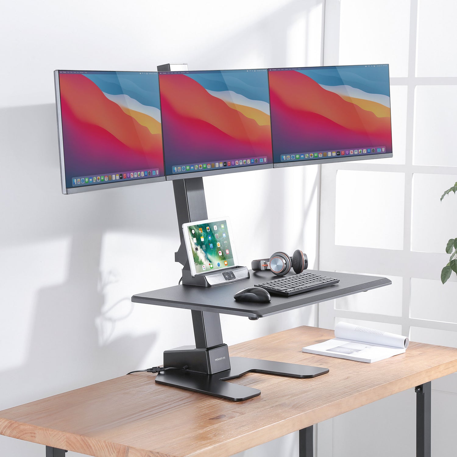 Wooden desk with a height-adjustable desk converter and three computer monitors on a white background