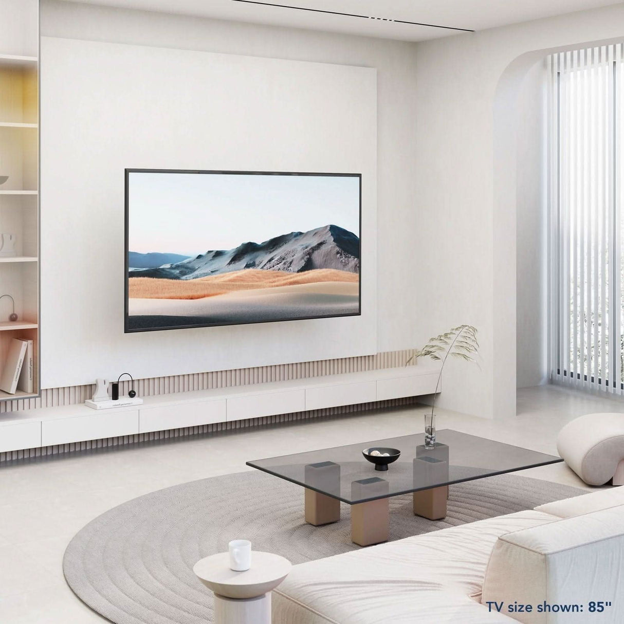 A modern living room features an 85" TV on the Mount-It! Heavy Duty Full Motion TV Wall Mount, with a desert scene, glass coffee table, curved beige sofa, minimalist decor, and floor-to-ceiling windows with vertical blinds.