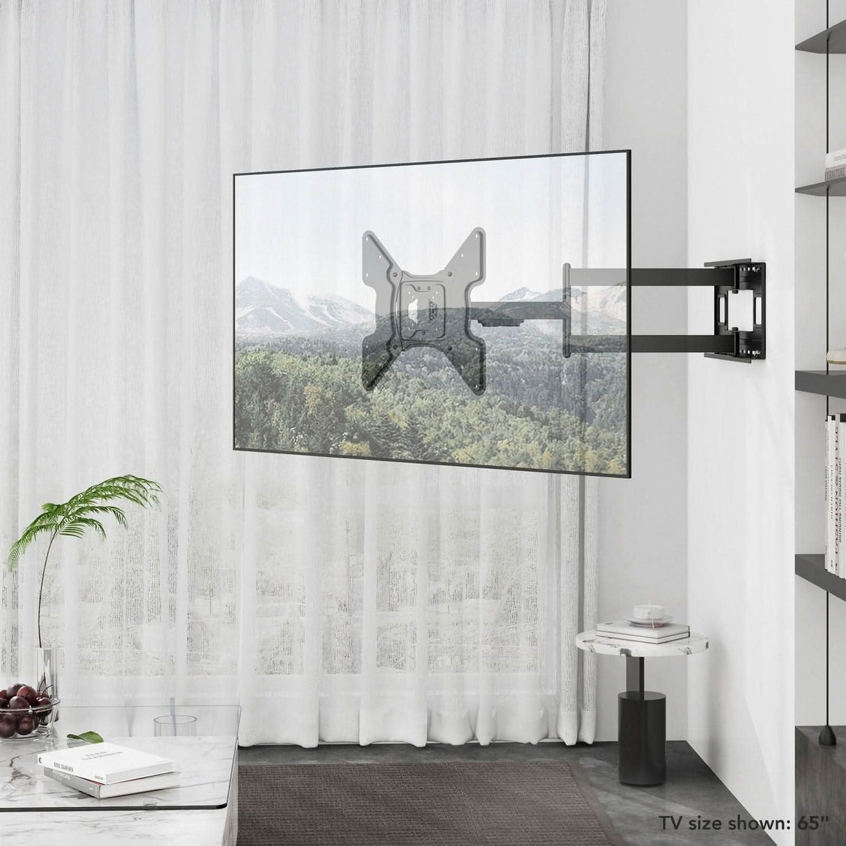 A Mount-It! Full Motion TV Wall Mount with Extra Long Extension holds a transparent TV (65"), displaying a mountain scene in a bright room with sheer curtains, a plant, round marble table, and modern decor.
