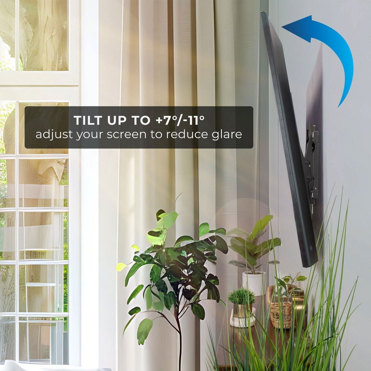 A Mount-It! Tilting TV Wall Mount supports tilt up to +7°/-11°, helping adjust your screen to reduce glare. VESA compatible. Shown here near a window with beige curtains and houseplants.