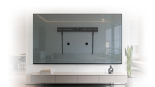 A minimalist living room with a low white TV stand, decor, and a wall-mounted TV bracket framed as art. A vintage clock hangs on the wall, and a cushion and ball are on the wooden floor.