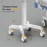 The Mount-It! MedHub Motorized Mobile Workstation, in white, features a compact base (20.5" x 21.4"), 7.6" legs, and four large 4" locking casters. It is shown on a gray floor next to a hospital bed.