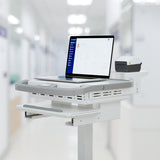 A Mount-It! MedHub Printer Holder mobile workstation with a laptop showing patient info and a compact printer on its shelf, set in a brightly lit hospital corridor.