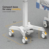 A close-up of the Mount-It! MedHub Mobile Workstation with Drawers, Powered, featuring a white height-adjustable base with four large lockable caster wheels (20.5" x 21.4", 7.6" wheel height) on a gray speckled floor next to a hospital bed.