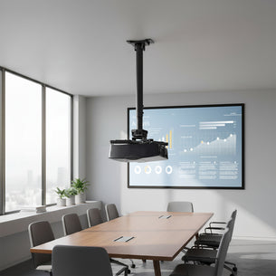 A modern conference room with a long wooden table, gray chairs, a large window, a digital display showing charts, and a Mount-It! Heavy Duty Projector Ceiling Mount securing the projector above the table.