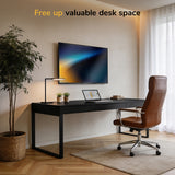 Modern home office with a black desk, brown leather chair, laptop, and monitor mounted on the Mount-It! Low-Profile Tilt TV Wall Mount. Sunlight through sheer curtains. Text at top: Free up valuable desk space.
