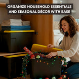 A woman smiles while organizing holiday decorations into the Mount-It! Heavy-Duty Storage Bin with Lid. Folded towels and stackable organizers are nearby. Text reads, Easily organize household essentials and seasonal décor.
