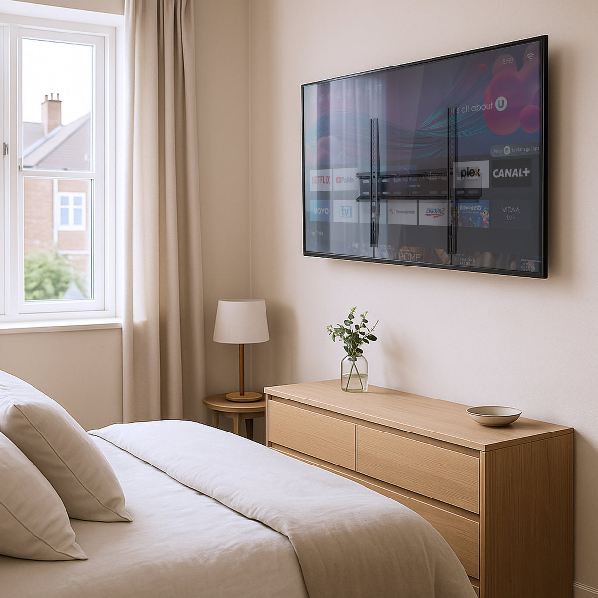 Modern bedroom featuring a flat-panel TV mounted with the Mount-It! Low Profile Slim TV Wall Mount Fixed TV Bracket, holding a 32-55 inch screen securely just over one inch from the wall for a sleek, space-saving look, with a light wood dresser, minimal decor, and natural light from a large window enhancing the clean, contemporary setup.