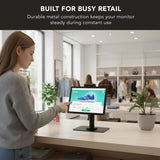 A person uses the Mount-It! Point-of-Sale Monitor Stand at a retail counter in a modern clothing store, with shelves and racks of clothes behind. Text highlights the stand’s durability for busy retail environments.