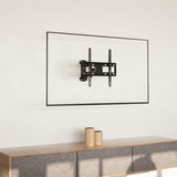 A Mount-It! Full Motion Corner TV Wall Mount is fixed to a plain white wall above a wooden cabinet with a gray fabric front. Two woven-pattern vases decorate the cabinet.