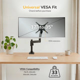 A Mount-It! Heavy Duty Monitor Desk Mount w/ USB & Multimedia Ports holds a monitor (17"–35", up to 33 lbs, universal VESA) on a tidy desk with a plant, mouse, and keyboard. Compatible with VESA mounts for versatile use.