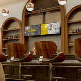 A modern bar with wooden chairs and bottle-lined shelves features an arched design behind the counter. Above, a Mount-It! Dual TV Ceiling Mount with Short Pole provides flexible cocktail menu displays. Pendant lights hang from the ceiling.