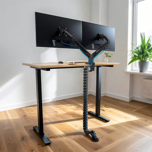 Cable Management Spine installed on a sit-stand desk organizing multiple cables from dual monitor arms to the floor, featuring flexible snap-together segments for adjustable height and protection, keeping the workspace neat and cables secure.