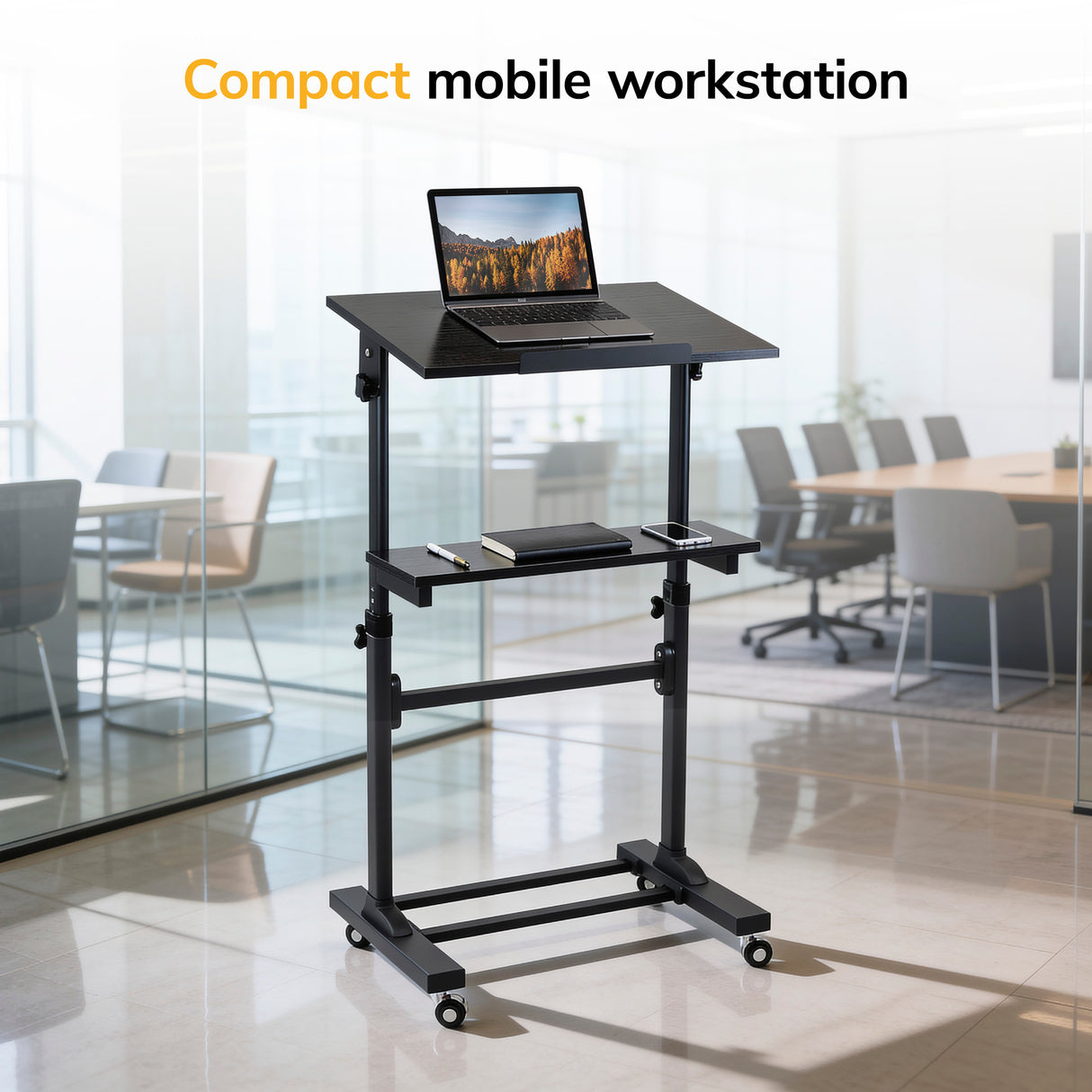 A Mount-It! Mobile Lectern Stand Up Desk in black holds a laptop, phone, and mug in a modern glass-walled office with a conference table. Text reads: Compact mobile workstation.
