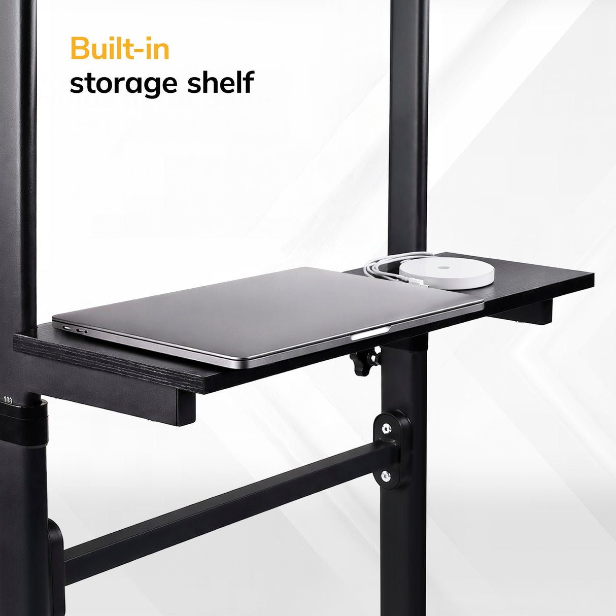 A close-up of the black built-in storage shelf on the Mount-It! Mobile Lectern Stand Up Desk, holding a closed laptop and wireless mouse, with “Built-in storage shelf” text in the upper left corner.
