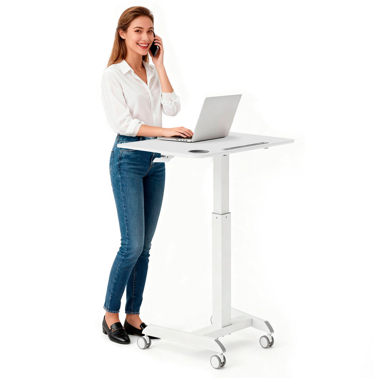 A woman smiles as she works on her laptop and talks on the phone at the Mount-It! Sit-Stand Mobile Laptop Cart, which features a height-adjustable design and wheels for easy movement. She's wearing a white shirt, blue jeans, and black shoes.