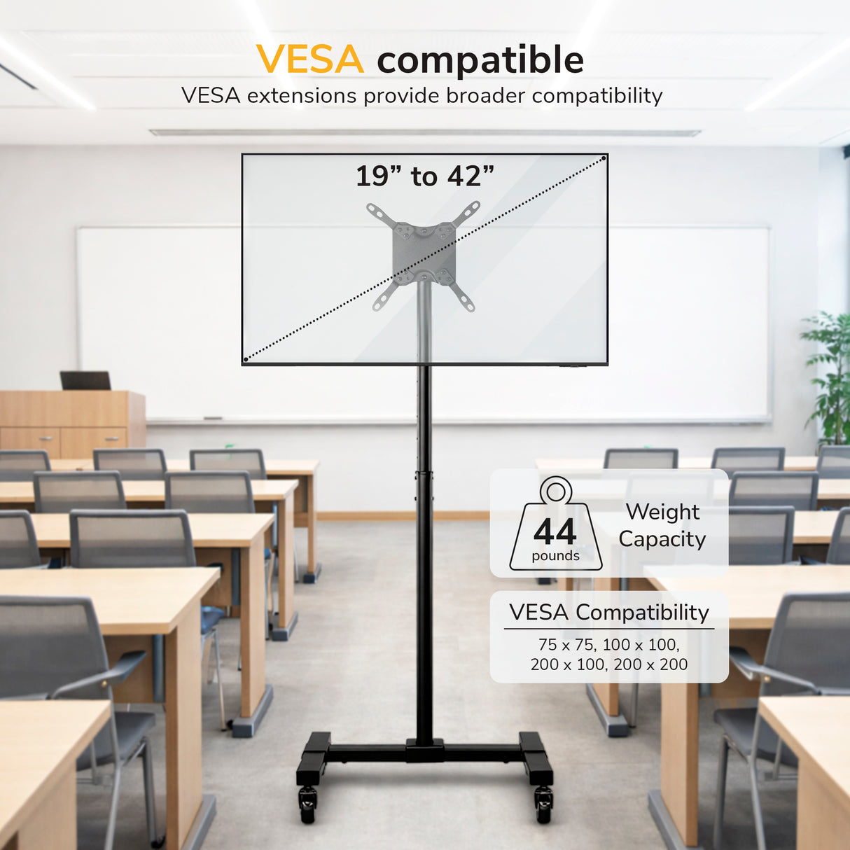 The Mount-It! Adjustable Mobile TV Stand with locking casters is set up in a classroom with desks and chairs. This mobile cart supports 19”–42” screens up to 44 lbs and is VESA compatible with various mounting patterns.